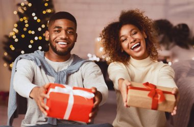 Noel hediyesi kutuları tutan ve Noel ağacının önünde gülümseyen siyah bir çift.