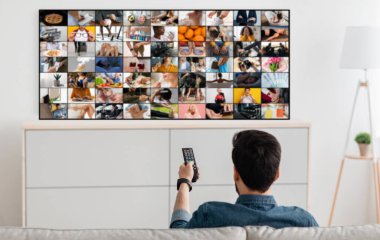 Bir adam kanepede oturuyor ve televizyon izliyor, uzaktan kumandayı elinde tutuyor. TV ekranı, her biri farklı bir sahne tasvir eden bir görüntü ızgarası gösteriyor.
