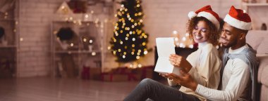 Mutlu afro çift Noel hediyesi kutusunu oturma odasında, Xmas ağacının önünde açıyor.