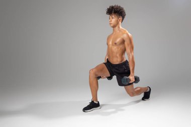 Genç bir adam her iki elinde dambıllar tutarken hareket egzersizi yapıyor. Odaklanmış durumda ve egzersiz sırasında formunu koruyor, kopyalama alanı.