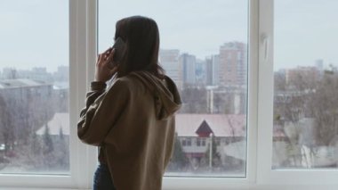 Karantina iletişimi. Cep telefonuyla konuşan genç bir kız, evin penceresinin yanında yürüyen, arkadan bakan.