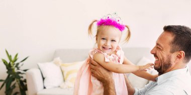 Küçük Peri. Evde babamla oynayan prenses gibi giyinmiş gülümseyen bir kız. Boş alan, seçici odak