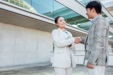 İki profesyonel erkek ve kadın çağdaş bir binanın dışında dostça tokalaşıyorlar. Açık bir gökyüzü ve parlak bir mimari zemin arasında iş meselelerini tartışıyor gibi görünüyorlar..