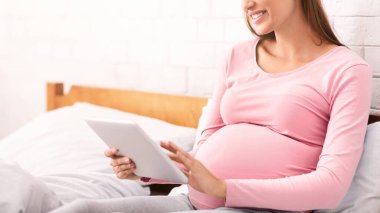 Hamilelik Tatili. Mutlu Hamile Kız Tablet Bilgisayar kullanarak Evde Yatakta Oturan İnternet 'i tarıyor. Seçici Odaklanma