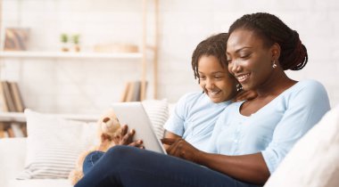 Sevgi dolu bir aile. Neşeli Afro-Amerikan anne ve kızı dijital tablet kullanarak internete göz atıyorlar. Boş alan