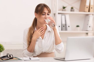 Boğaz ağrısı. Hasta ofis kızı, bir bardak su içiyor. Boynuna dokunuyor. İş yerinde dizüstü bilgisayarda oturuyor..