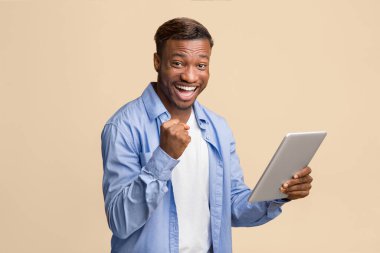 Afro-Amerikalı neşeli adamın elinde dijital tablet var. Evet, sarı arka planda duruyor. Stüdyo Çekimi