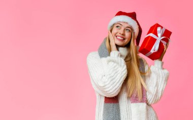 Kırmızı Noel Baba şapkalı mutlu sarışın kız elinde hediye kutusuyla fotokopi odasına bakıyor.