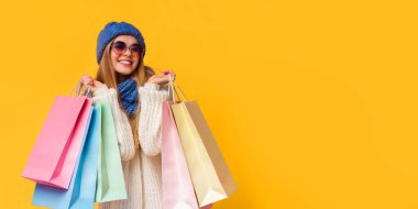 Season of sales. Happy young woman in knitted hat and sunglasses with shopping bags, pink studio background, panorama with empty space