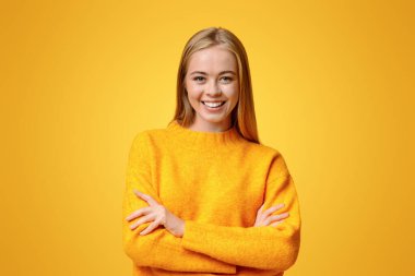 Kameraya poz veren güzel bir genç kızın portresi. Kollarını katlamış, turuncu arka plan üzerinde boş alan var.