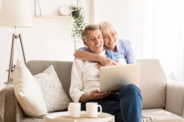 Счастливая пожилая пара, имеющая видео-звонок на ноутбуке, разговаривающая с внуками и улыбающаяся
