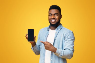 Yakışıklı Afro-Amerikalı adam siyah ekranlı akıllı telefon gösterisi yapıyor ve üzerine işaret ediyor, sarı arka plan ve boş alan.