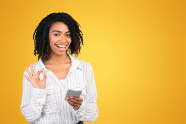 Teknoloji Konsepti. Elinde cep telefonu olan tatmin olmuş siyahi bir kadın beyaz arka planda izole edilmiş iyi niyet göstergesi gösteriyor.