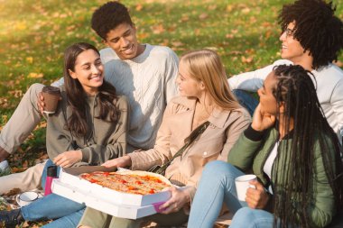 Pizza alıp götüren bir grup etnik kökenli genç yerde oturup hafta sonunun tadını çıkarıyorlar.