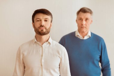 Ciddi bir orta yaşlı oğul ve yaşlı babası beyaz arka plandaki kameraya bakıyor. Seçici Odaklanma