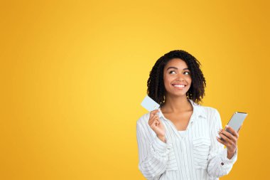 Çevrimiçi ödeme. Kredi kartı tutan siyah bir kadın, online alışveriş için cep telefonu kullanıyor, fotokopi alanına bakıyor.