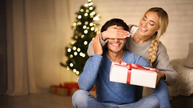 Kocasına Noel sürprizi yapan neşeli bir kadın, gözlerini arkadan kapatıyor.