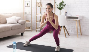 Evde çalışmaya devam et. Mutlu milenyum kızları, aydınlık odada yoga minderinde hamleler yapıyor.