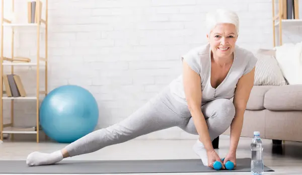 stock image Active senior woman warming up, doing legs stretching exercises at home, panorama with empty space