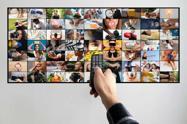 stock image A persons hand is shown holding a remote control, pointing at a television screen. The television screen displays a collage of various images, each depicting a different activity or scene.