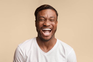 Lol. Duygusal Afro-Amerikan adam yüksek sesle sarı arka plan üzerinde stüdyoda duran kamera bakarak gülüyor.