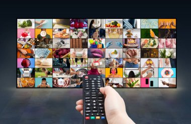 Bir insan eli büyük bir televizyon ekranının önünde siyah bir uzaktan kumanda tutar. Televizyon ekranında çeşitli sahne ve etkinlikleri gösteren çok sayıda renkli resim yer alıyor.