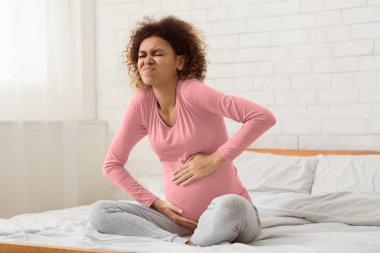 Doğum sancıları. Hamile bir kadın karın ağrısı çekiyor, yatakta oturuyor ve doğum yapmaya hazırlanıyor.