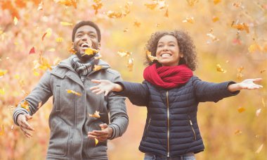 Sonbahar yapraklarını atan mutlu afro çift parkta yürüyor ve eğleniyor.