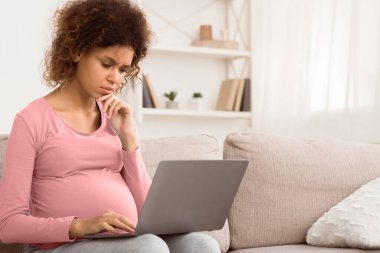 Karmaşık afro beklenen kadın dizüstü bilgisayar kullanıyor, yeni doğan bebek için bir şeyler alıyor, boş yer var.