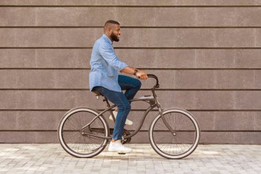 Ofise giden yol. Genç Afrikalı Amerikalı iş adamı bisiklet sürüyor, arka planda şehir duvarına karşı, işe gidiyor.