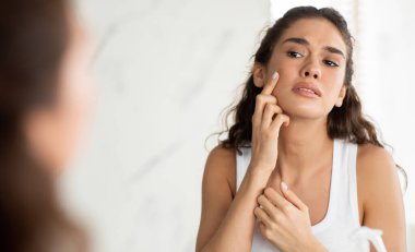 Skin Problem. Depressed Woman Touching Pimple On Face Looking At Mirror In Modern Bathroom. Facial Skin Issues, Medical Care And Treatment Concept. Selective Focus