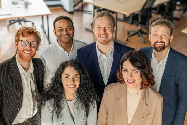 stock image Five diverse business professionals stand together in a modern office, looking directly at the camera and smiling. They are wearing business casual attire, high angle view