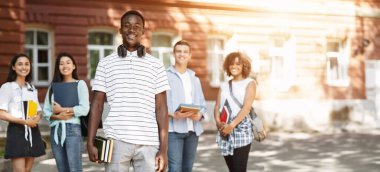 Üniversiteden arkadaşlarıyla kampüste poz veren mutlu Afrikalı Amerikalı öğrenci seçici bir şekilde Afro Guy 'a odaklanıyor.