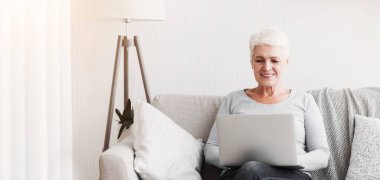 Hırslı kıdemli iş kadını evdeki kanepede dizüstü bilgisayar kullanıyor.