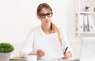 Evrak işi kavramı. Ciddi iş kadını rapor okuyor ve modern ofiste dizüstü bilgisayarda oturarak not alıyor..