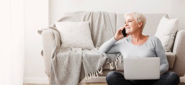 Neşeli yaşlı iş kadını evdeki müşterilerle konuşuyor, yerde oturuyor ve dizüstü bilgisayar kullanıyor, boş yer var.