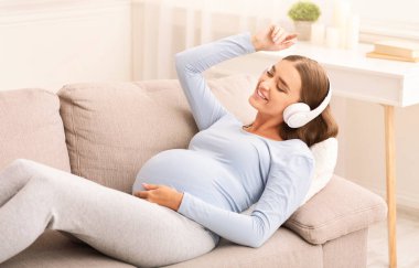 Hamilelik Çalma Listesi. Kulaklıklı Mutlu Bekleyen Kız Evde koltukta uzanan müzikten zevk alıyor