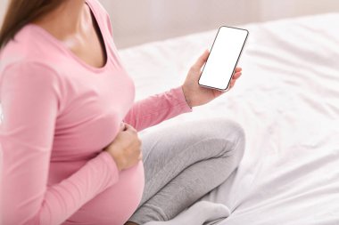 Hamilelik Uygulamaları. Yatağında boş ekranı olan, cep telefonu tutan, tanınmayan hamile bir kadın. Model, Kırpılmış
