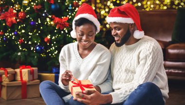 Xmas Darling ile evlen. Afrikalı Amerikalı çift Noel 'i evde kutluyor, erkek kız arkadaşına hediye veriyor..