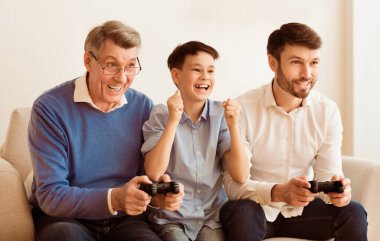 Heyecanlı çocuk, baba ve büyükbaba video oyunları oynuyorlar evde koltukta otururken eğleniyorlar. Seçici Odaklanma