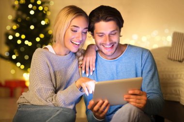 Tabletteki eski fotoğraflara bakan çift Noel ağacının yanında oturuyor.