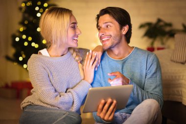 Mutlu çift Noel arifesinde tabletten film seçiyor, evde birlikte dinleniyorlar.