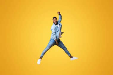 Uzun boylu, komik siyahi bir adam sarı stüdyo arka planına doğru yükseliyor. Boşluğu kopyala.