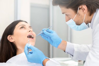 Modern diş kliniğinde kontrol yapan genç bir kadın, dişlerini kontrol eden yakışıklı bir doktor.