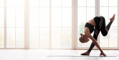 Evde yoga yapan genç bir kadın. Alnıyla dizine dokunuyor. Yoga minderinde kalıyor.