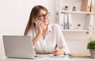İş İletişimi. Modern ofiste dizüstü bilgisayarın başında oturan mutlu iş kadını konuşuyor..
