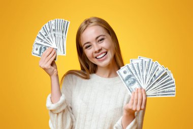 Genç yatırımcı. Turuncu arka planda bir sürü dolar tutan mutlu bir milenyum kızı.