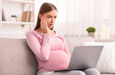 Bilgisayarlı endişeli hamile kadın, internette geziniyor. İçerideki koltukta oturan şok edici haberleri okuyor. Hamilelik Korkusu ve Endişesi. Seçici Odaklanma