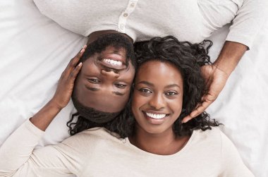 Romantik Afro-Amerikan çifti yatakta birlikte yatarken, birbirlerine nazikçe dokunurken, kameraya gülümserken, yakın çekim yaparken.