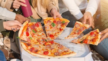 Uluslararası arkadaş grubundan eksilmiş eller pizza alıyor, piknik yapıyorlar.